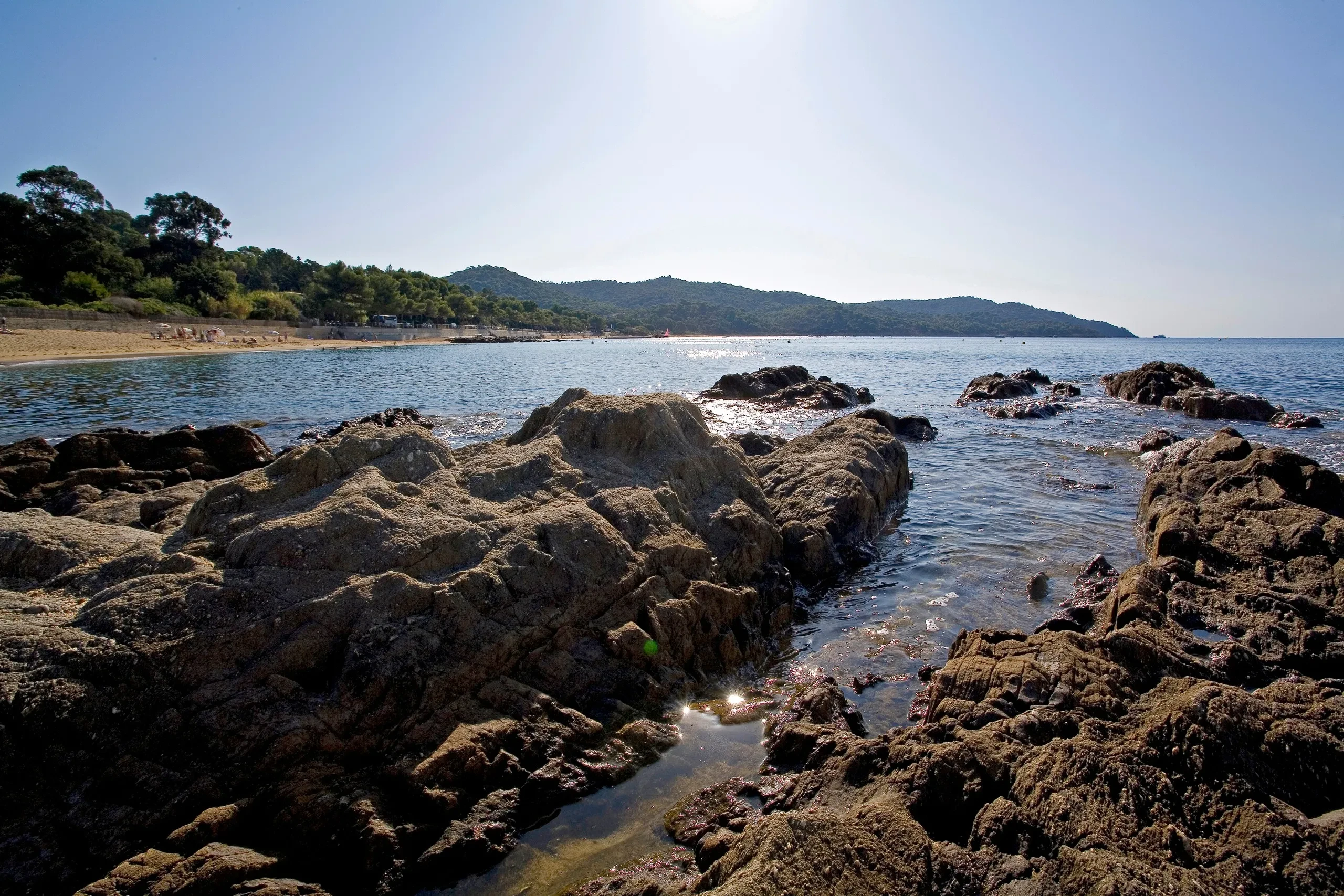 Plage rocheuse avec mer et montagnes en arrière-plan.